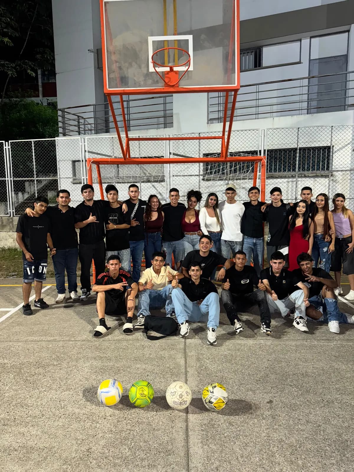 Grupo reunido de noche en una cancha, frente al arco y el tablero